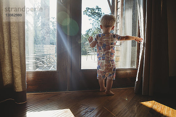 Rückansicht eines kleinen Jungen  der zu Hause durch eine Glastür schaut