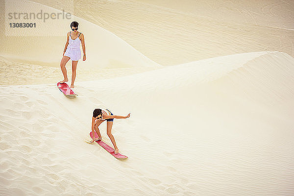 Hochwinkelaufnahme von Schwestern beim Sandboarding in der Wüste