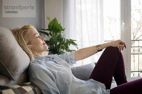 Seitenansicht einer entspannten Frau  die Musik hört  während sie zu Hause auf dem Sofa sitzt