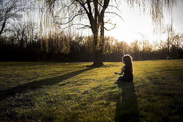 Mädchen sitzt bei Sonnenuntergang auf Grasfeld