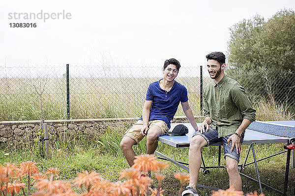 Glückliche männliche Freunde sitzen auf dem Tennistisch im Hof