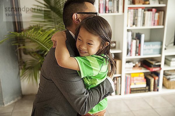 Lächelnde Tochter umarmt Vater  während sie zu Hause im Wohnzimmer steht