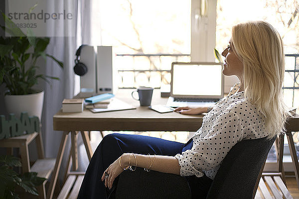 Seitenansicht einer nachdenklichen Frau  die im Heimbüro auf einem Stuhl sitzt