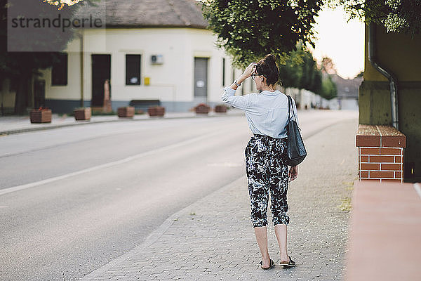 Rückansicht einer Frau  die eine Handtasche trägt  während sie auf dem Bürgersteig in der Stadt steht