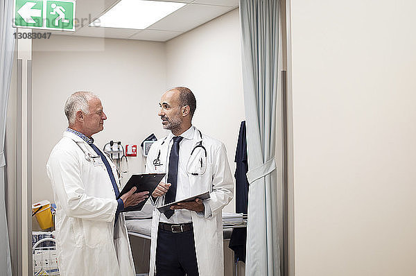 Ärzte diskutieren medizinische Berichte  während sie im medizinischen Untersuchungsraum stehen