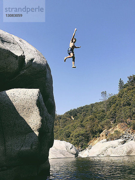 Niedrigwinkelaufnahme eines sorglosen Jungen ohne Hemd  der im Yuba River von einer Klippe springt