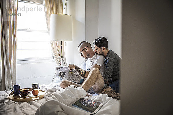 Schwule Männer lesen Zeitung  während sie zu Hause im Bett sitzen