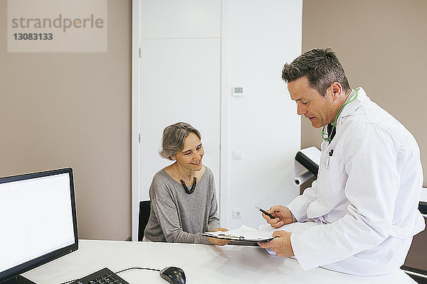 Glücklicher Arzt und Patient schauen auf die Zwischenablage  während sie in einer medizinischen Klinik sitzen
