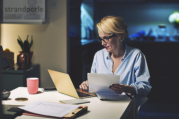 Geschäftsfrau mit Dokument  die bei der Arbeit zu Hause einen Laptop benutzt