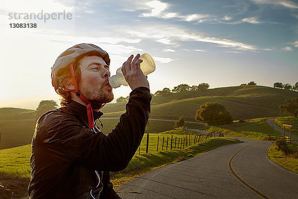 Mann mit Helm beim Trinken von Wasser gegen den Himmel