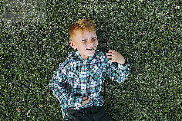 Draufsicht auf den glücklichen Jungen  der auf einem Grasfeld im Park liegt
