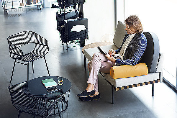 Hochwinkelansicht eines Geschäftsmannes mit einem Tablet-Computer  während er im Büro auf dem Sofa sitzt