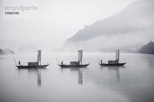 Männer rudern traditionelle chinesische Boote bei nebligem Wetter auf dem See