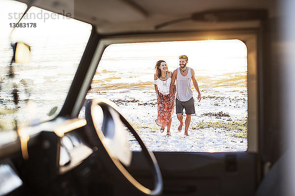 Fröhliches  am Strand spazierendes Paar durch das Fenster eines Geländewagens gesehen