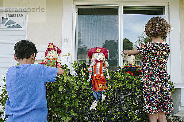 Rückansicht von Geschwistern  die im Garten Spielzeug auf Pflanzen legen