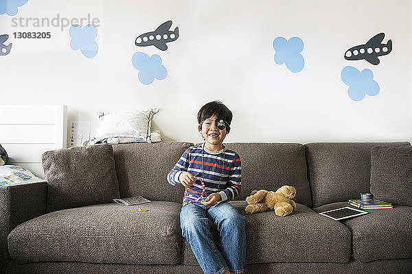 Glücklicher Junge spielt zu Hause auf dem Sofa mit Spielzeug