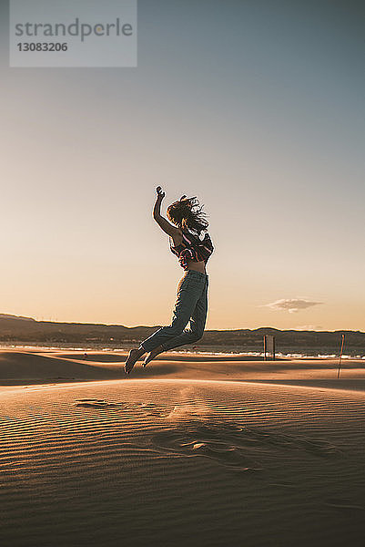 Glückliche Frau springt bei Sonnenuntergang am Strand gegen den Himmel