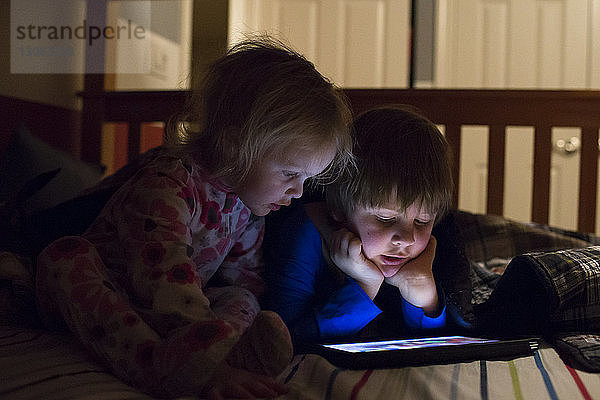 Geschwister benutzen Tablet-Computer zu Hause am Bett