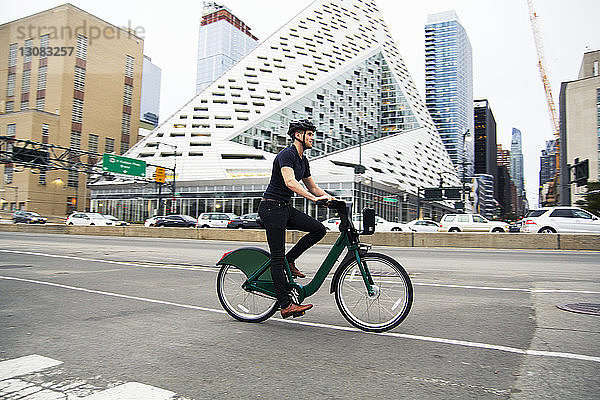 Fahrrad fahrender Mann in voller Länge auf der Straße bei Gebäuden in der Stadt