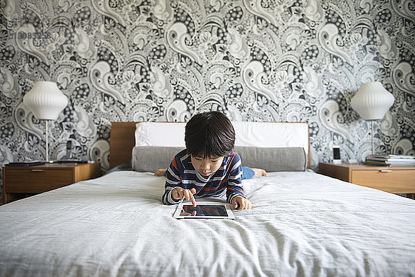 Auf dem Bett liegender Junge  der ein digitales Tablett im Schlafzimmer benutzt