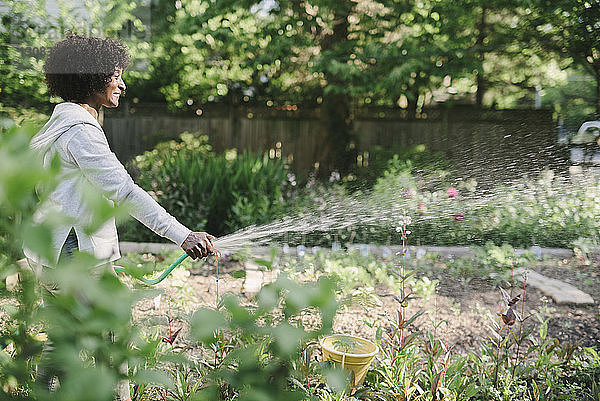 Seitenansicht einer reifen Frau  die Pflanzen im Garten gießt