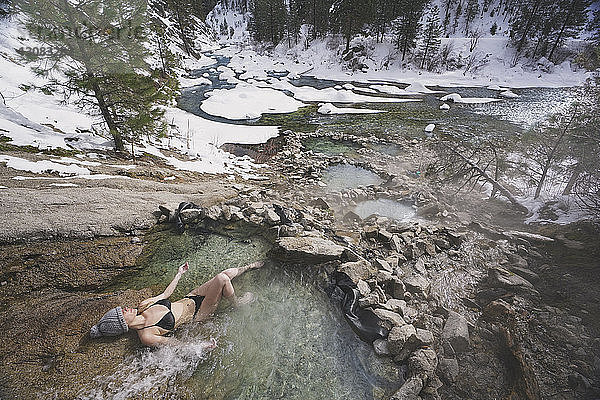 Hochwinkelaufnahme einer Frau im Bikini  die sich im Winter im Thermalbad im Wald entspannt