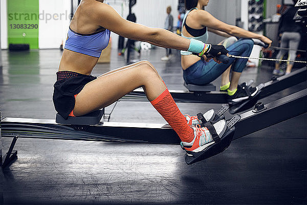 Seitenansicht von entschlossenen Sportlerinnen mit Rudergerät im Fitnessstudio