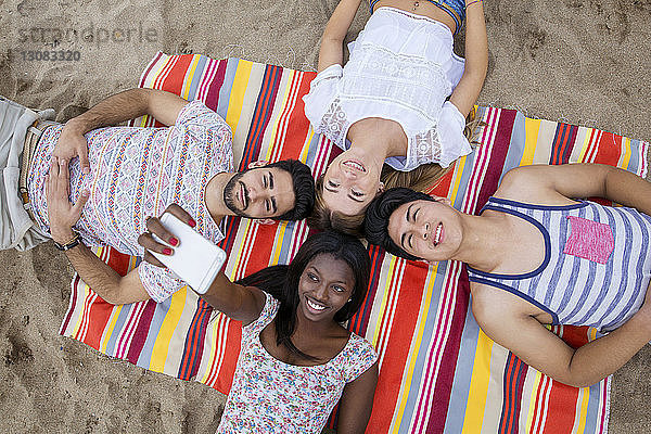 Draufsicht auf multi-ethnische Freunde  die sich am Strand zusammenkauern