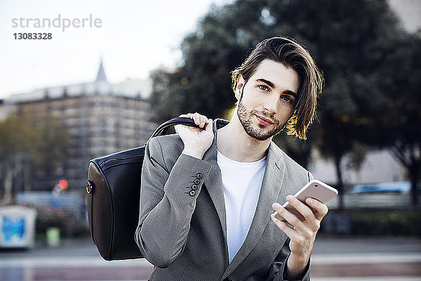 Porträt eines Geschäftsmannes  der bei der Benutzung eines Mobiltelefons eine Tasche trägt