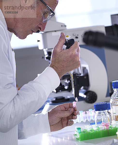 Seitenansicht eines männlichen Wissenschaftlers beim Pipettieren von Proben in einem Fläschchen auf einem Labortisch