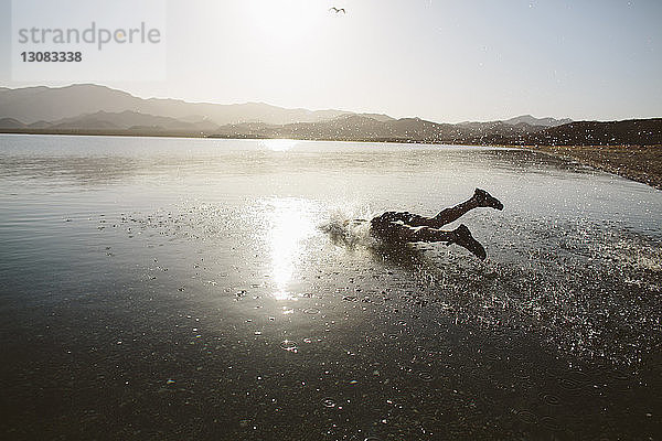 Sorgloser Mann springt bei Sonnenschein gegen klaren Himmel in den See