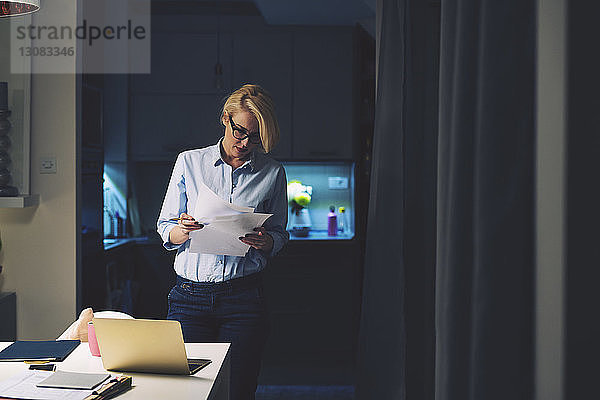 Geschäftsfrau liest Dokumente  während sie im Heimbüro am Schreibtisch steht