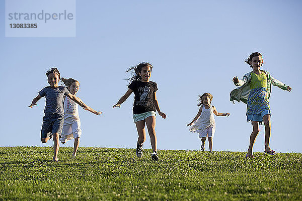 Glückliche Geschwister rennen auf Grasfeld gegen klaren blauen Himmel im Park