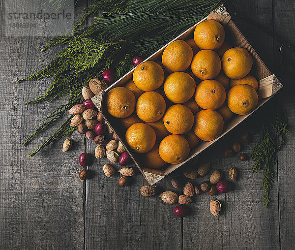 Hochwinkelansicht von Orangen in Kiste nach verschiedenen Trockenfrüchten und Pflanzen auf Holztisch