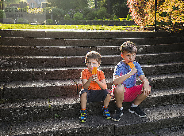 Jungen essen Eis am Stiel  während sie auf Stufen sitzen