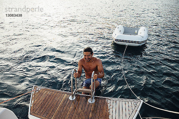 Glücklicher nasser Mann klettert auf die Leiter eines Bootes