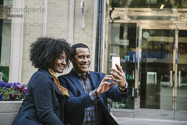 Glückliches Paar  das sich über ein Smartphone selbstständig macht  während es in der Stadt auf seinem Platz sitzt