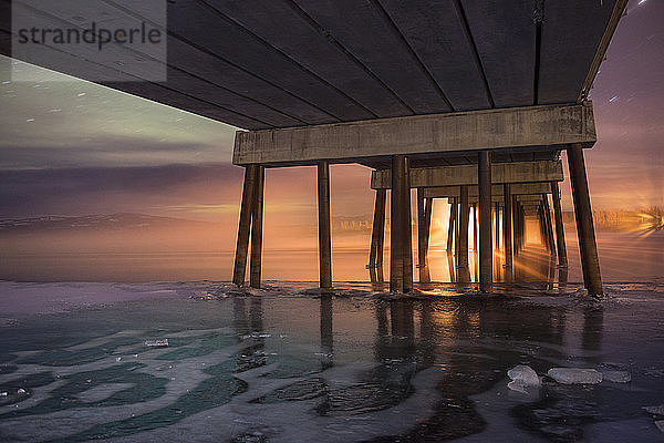 Niedrigwinkelansicht des Piers über dem zugefrorenen Meer bei Sonnenuntergang
