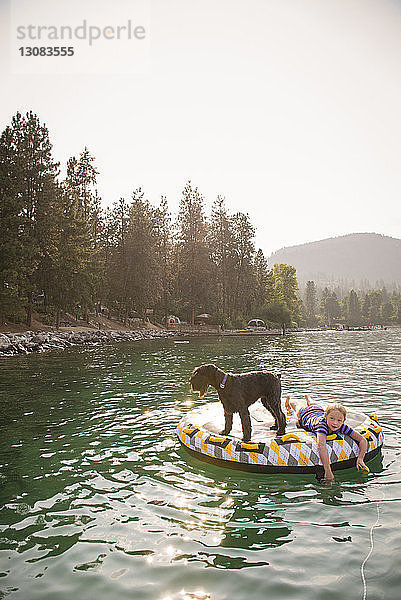 Mädchen mit Hund liegt auf einem Floß im See vor klarem Himmel