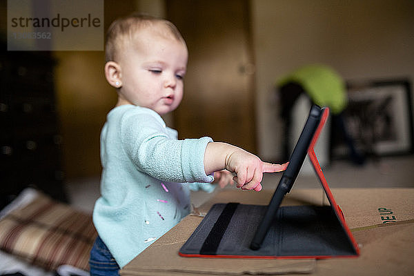 Hübsches Mädchen benutzt Tablet-Computer  während es zu Hause an der Kiste steht