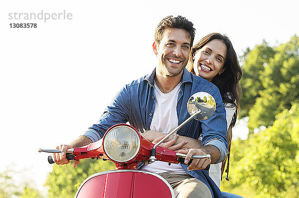Glückliches Paar fährt auf einem Motorroller gegen den klaren Himmel