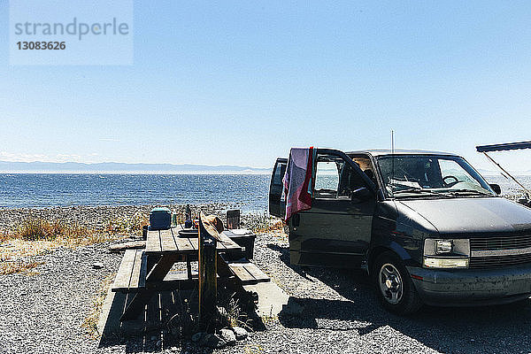 Picknicktisch und offenes Auto am Ufer gegen das Meer und den klaren Himmel am sonnigen Tag