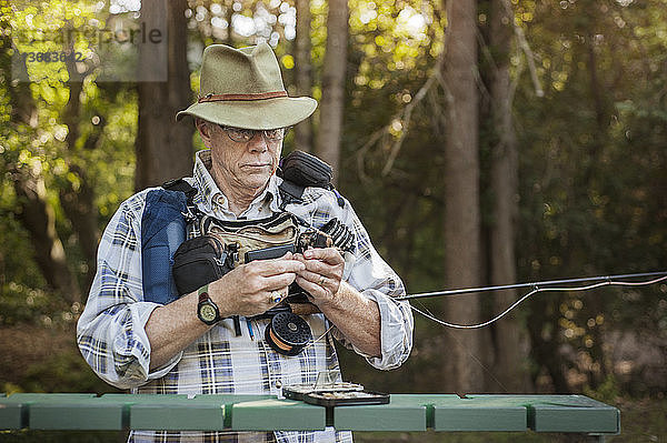 Älterer Mann untersucht Angelrute im Wald