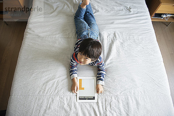 Hochwinkelansicht eines lächelnden Jungen mit digitalem Tablett am Bett