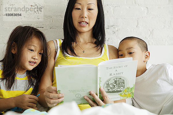 Mutter liest Kindern ein Buch vor  während sie zu Hause im Bett sitzt