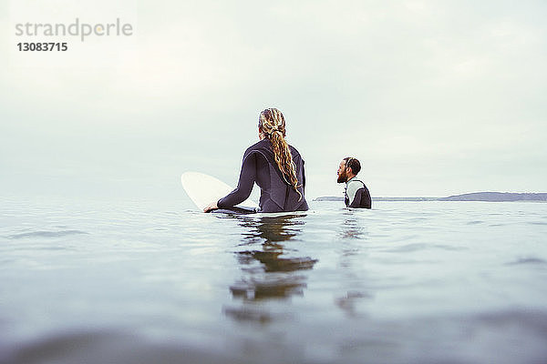 Männliche und weibliche Surfer entspannen sich im Meer vor bewölktem Himmel