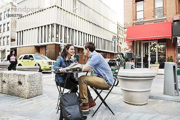Ehepaar sitzt am Tisch an der Straße gegen Gebäude in der Stadt