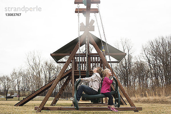 Verspielte Geschwister schwingen auf dem Spielplatz gegen den klaren Himmel