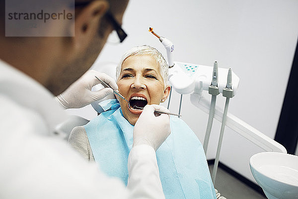 Männlicher Zahnarzt untersucht die Zähne des Patienten in der Klinik