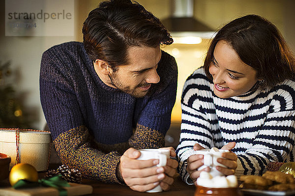 Lächelndes Paar mit Marshmallow-Kaffee bei Tisch zu Weihnachten